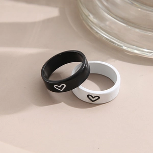 Minimalist black and white couple rings with heart pattern on a warm beige surface