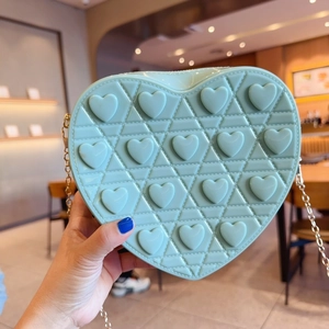 Detail of mint green heart-shaped jelly bag with quilted texture and gold chain strap
