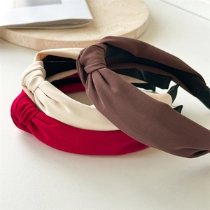 Close-up of three knotted fabric headbands in brown, beige, and red on a stone tray