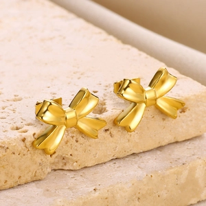 Close-up of polished 18K gold-plated stainless steel bow earrings on a stone base