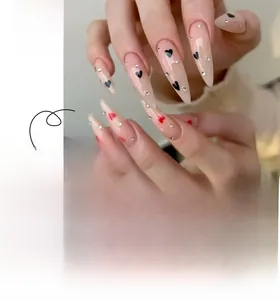 Detail view of nude stiletto press-on nails with black and red heart patterns and rhinestones