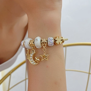 Detail of a gold-tone wire bracelet featuring star and moon charms with colorful rhinestones