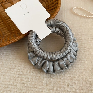 Détail d'un chouchou en satin plissé gris avec texture de soie sur un fond en peluche