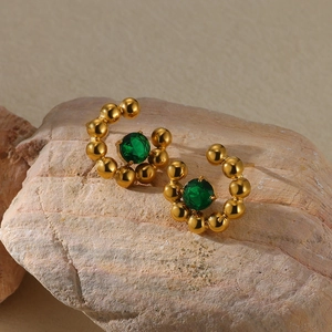Detail of C-shaped gold beaded earrings with a large emerald green center gemstone
