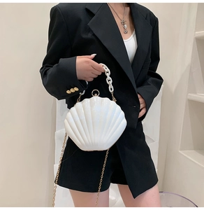 Detailed shot of white shell-shaped acrylic handbag with white chain and gold strap