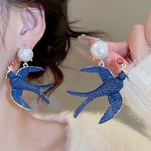 Detail of blue swallow drop earrings with white pearl and small red rose accents