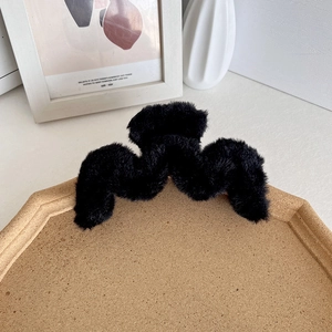 Plush black faux fur shark hair claw clip with wavy design on a cork display stand