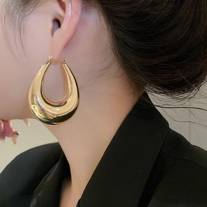 Close-up of polished gold water drop hoop earrings worn by a model in a luxury style