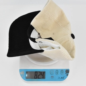Detail shot of corduroy baseball cap weighing 82.4g on a white scale for weight reference