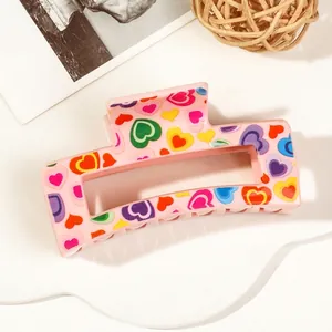 Detail of pink rectangular hair claw clip featuring vibrant multicolored heart patterns