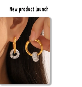 Detail of gold titanium steel hoop earrings with elegant marble stone pendants worn by model