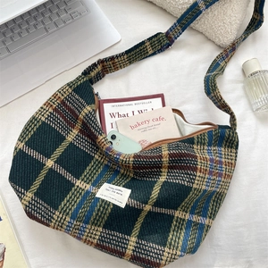 Flat lay view of a large plaid crossbody bag with books and laptop for lifestyle context