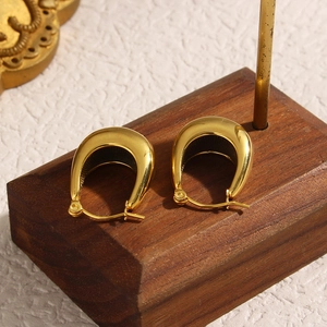 Detailed view of gold hollow U-shaped stainless steel hoop earrings on a wooden stand