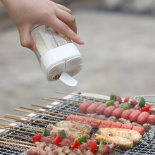 Close-up of hand using clear spice shaker with white lid over grilled BBQ skewers
