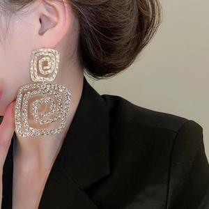 Detail of gold wrinkled square earrings showing textured metal finish on a female model