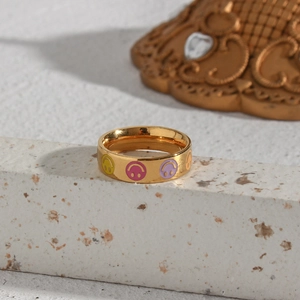 Close-up of golden stainless steel ring with colorful enamel smiley faces on a stone pedestal