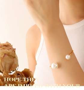 Detailed view of an elegant open cuff bracelet with two pearls on a gold-plated band