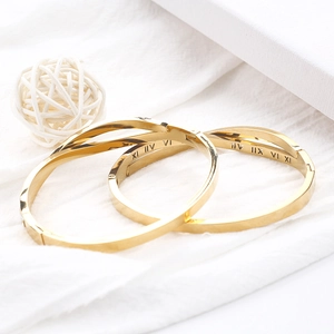 Détail de deux bracelets croisés dorés avec chiffres romains sur fond de textile blanc