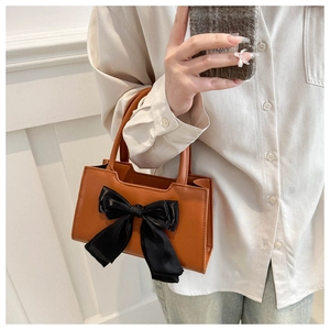 Detail view of mini caramel leather handbag with a large black satin bow accessory