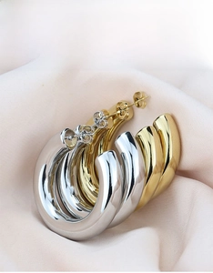 Close-up of gold and silver hollow C-shaped hoop earrings on soft pink silk background