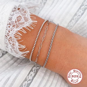 Detail van 925 sterling zilveren paperclip-, kralen- en gedraaide schakelarmbanden om de pols
