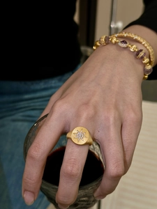 Detailed close-up of a gold-plated star signet ring held with a wine glass for luxury vibes