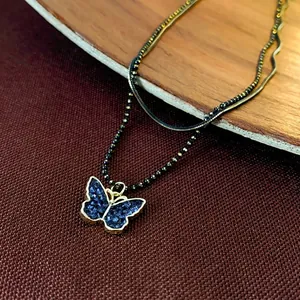 Double-layer necklace with blue butterfly pendant and black beads on a wooden background