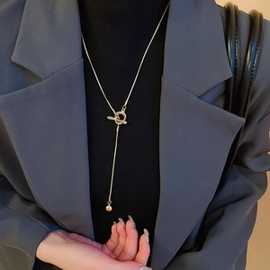 Detail of a minimalist golden OT buckle necklace with a small round ball pendant