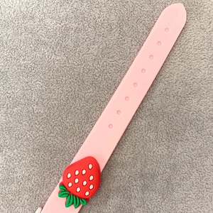Detailed view of pink silicone watch strap with 3D strawberry decoration and adjustable holes