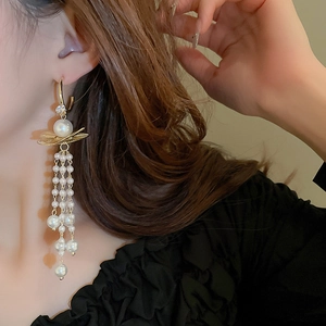 Boucles d'oreilles élégantes en perles avec feuilles d'or portées sur l'oreille d'un modèle