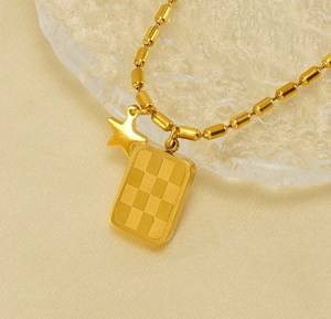 Dettaglio della collana in acciaio dorato con ciondolo a scacchi e stella su vassoio