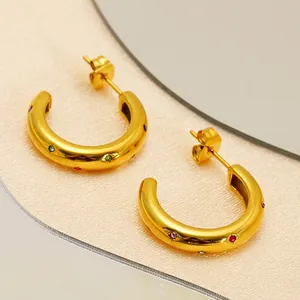 Golden C-shaped hoop earrings with colorful zircon stones on a pearl textured background