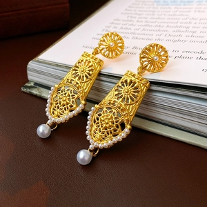 Detail of vintage gold hollow flower earrings with delicate pearls on a book background