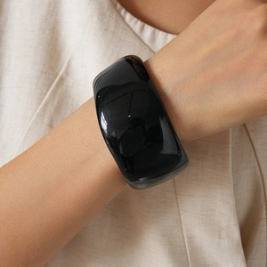 Polished black acrylic wide cuff bracelet worn by a model against a beige background