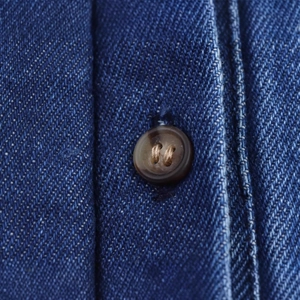 Detailansicht eines blauen Denim-Kimono-Hemdes mit Stoffstruktur und braunem Knopf