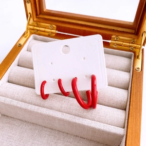Detail view of red geometric hoop earrings on a white card inside a wooden jewelry box
