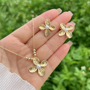 Gold four-petal flower jewelry set with brushed metal texture and central pearl accent