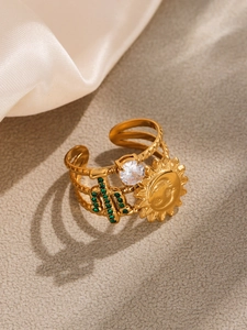 Detail view of gold cactus ring with green zircon and sun emblem on matte surface