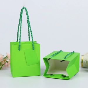 Detail view of a green paper gift bag showing sturdy square bottom and twisted rope handle