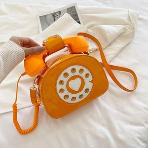 Detail of creative vintage telephone shaped crossbody bag in glossy orange patent leather