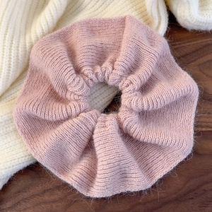 Detail of pink knitted ruffled scrunchie with soft wool texture on a wooden surface