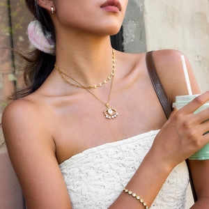Close-up of a double-layered gold Evil Eye necklace with pearls on a female model