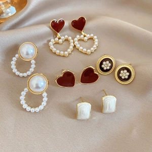 Detailed set of vintage pearl and crystal stud earrings displayed on elegant champagne silk