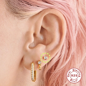 Detail of 925 sterling silver gold earrings set with zircons worn on model's ear