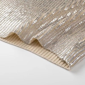 Close-up of beige ribbed knit fabric featuring shimmering silver sequins texture