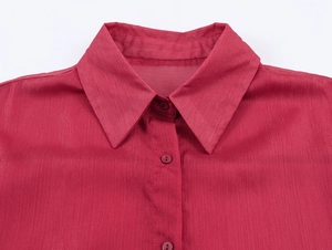 Détail du col d'une chemise en mousseline rouge avec boutons et texture métallique fine