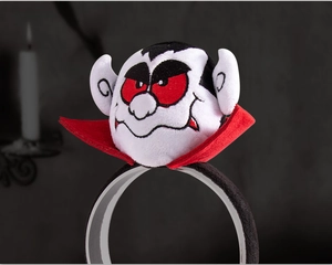 Detail of Halloween vampire headband featuring a plush doll with red cape on dark background