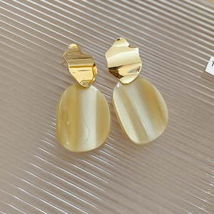 Detail of irregular gold metal and beige marble resin drop earrings on tray