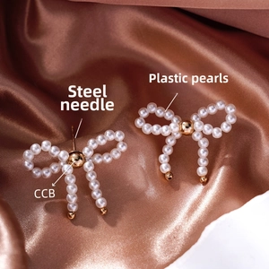 Detail of elegant bow earrings with pearls and gold fringe on silk background