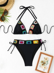 Flat lay of black crochet bikini with colorful floral embroidery and vacation accessories